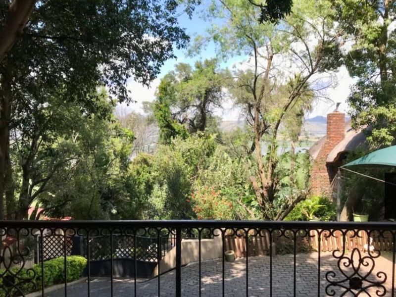 A raised balcony area featuring wrought iron railings and brick paving, overlooking a lush garden and mature trees.