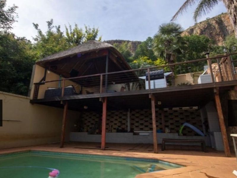 Outdoor pool area featuring a raised timber deck with a thatched lapa, overlooking a swimming pool with paved surrounds and retaining wall structure.