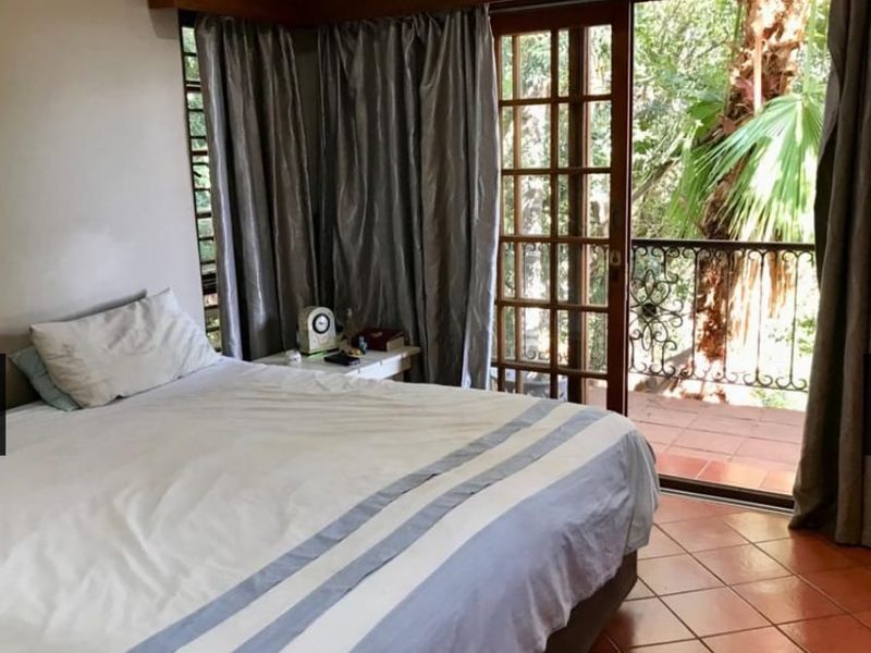 Bedroom featuring terracotta floor tiles and a wooden framed sliding door leading to a private balcony with wrought iron railing.
