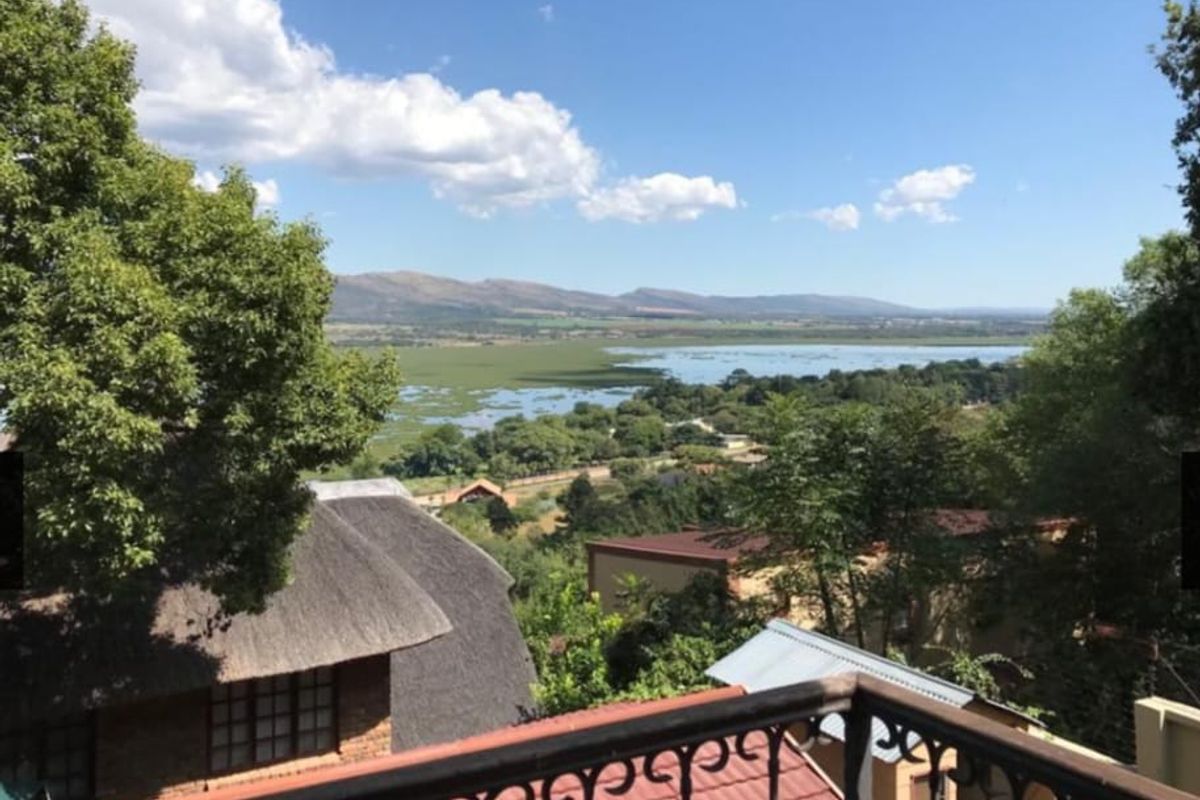 Elevated outdoor view overlooking a scenic landscape with a lake and distant mountains, framed by a wrought iron balcony railing.