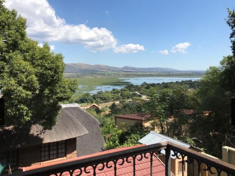 Elevated outdoor view overlooking a scenic landscape with a lake and distant mountains, framed by a wrought iron balcony railing.