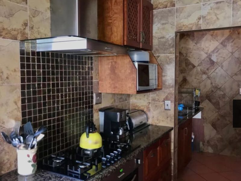 A functional kitchen featuring granite countertops, wooden cabinetry, a gas hob with extractor fan, and a tiled backsplash, with an adjacent scullery area.