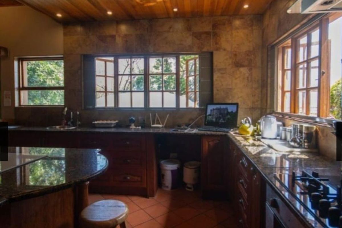 A rustic kitchen featuring timber ceilings, granite countertops, wooden cabinetry, and terracotta flooring, offering a warm and traditional aesthetic.