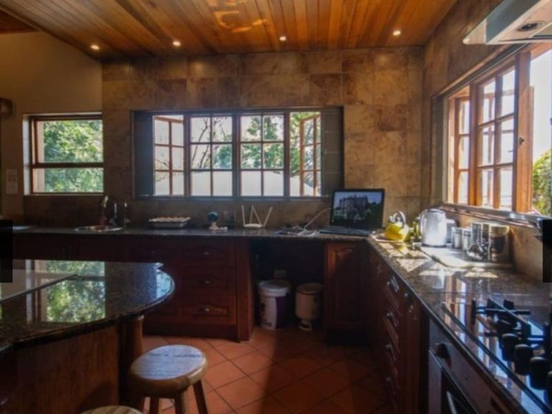 A rustic kitchen featuring timber ceilings, granite countertops, wooden cabinetry, and terracotta flooring, offering a warm and traditional aesthetic.