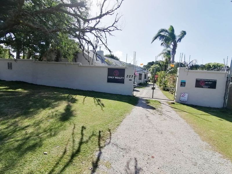 Front view of the property featuring a gravel driveway, secure perimeter wall with electric fencing, and a metal entrance gate.