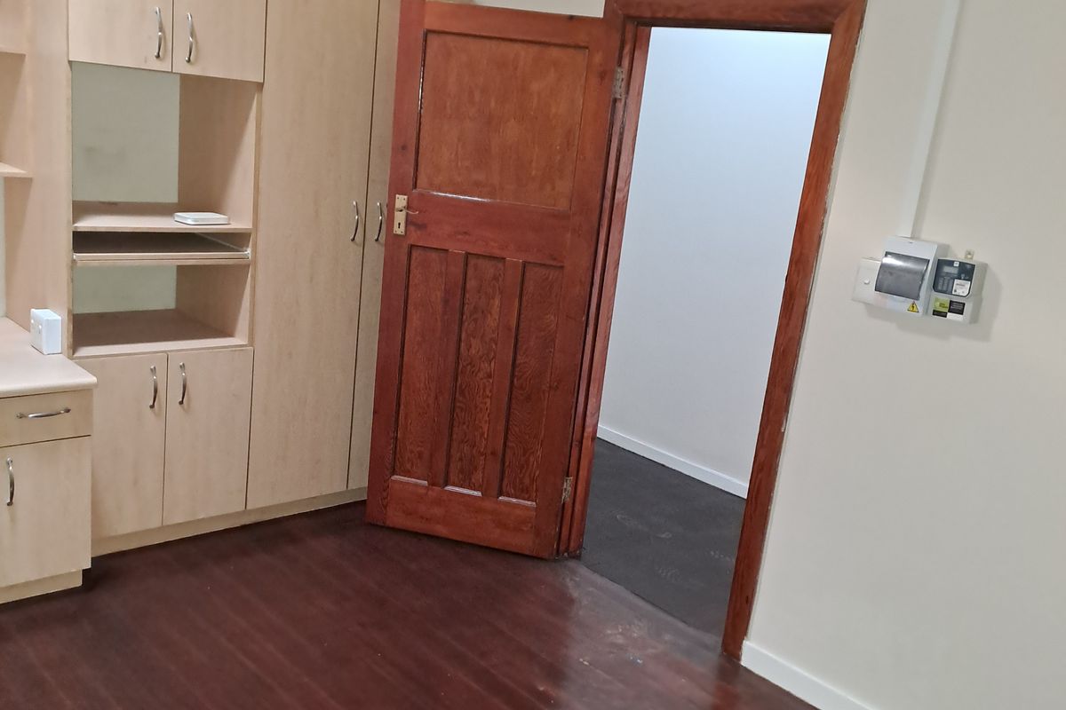 An empty bedroom featuring timber flooring, a wooden door, and built-in cabinetry, providing a functional space ready for personalization.