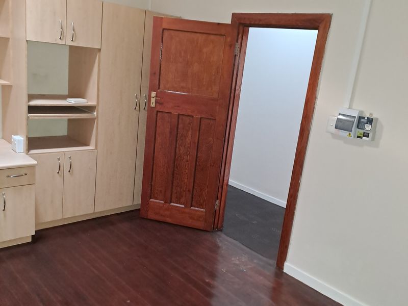 An empty bedroom featuring timber flooring, a wooden door, and built-in cabinetry, providing a functional space ready for personalization.