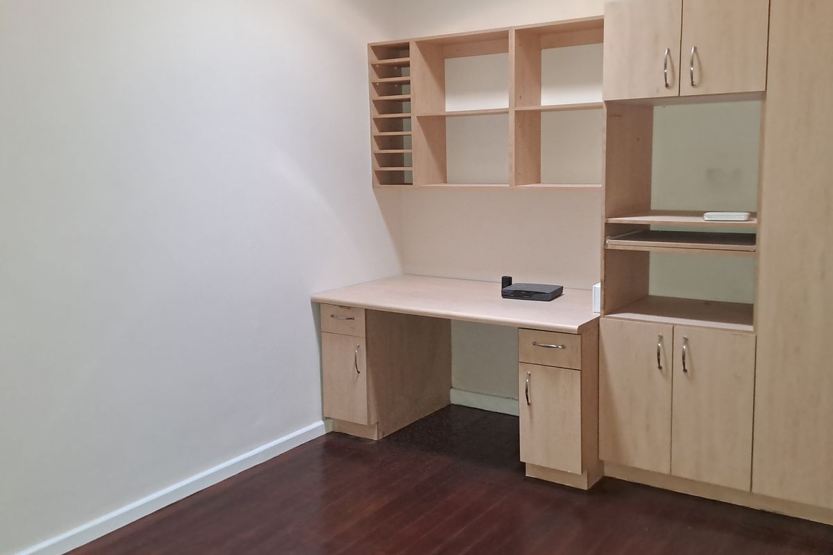 A dedicated home office space featuring built-in wooden cabinetry, shelving, and a desk, complemented by dark laminate flooring.