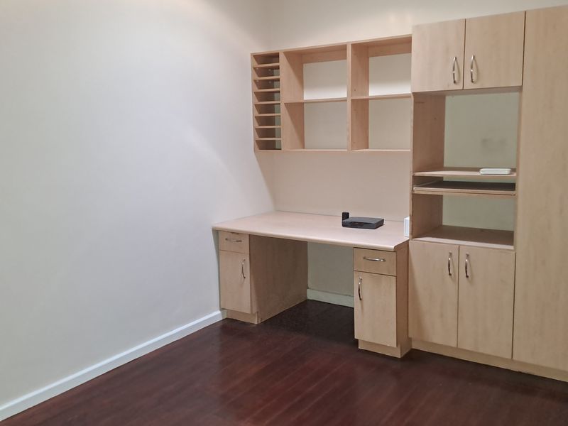 A dedicated home office space featuring built-in wooden cabinetry, shelving, and a desk, complemented by dark laminate flooring.
