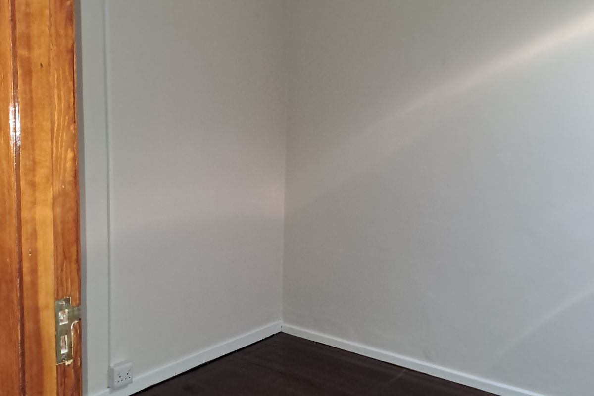 A close-up view of a corner showing a wooden door frame, white walls, and dark laminate flooring.