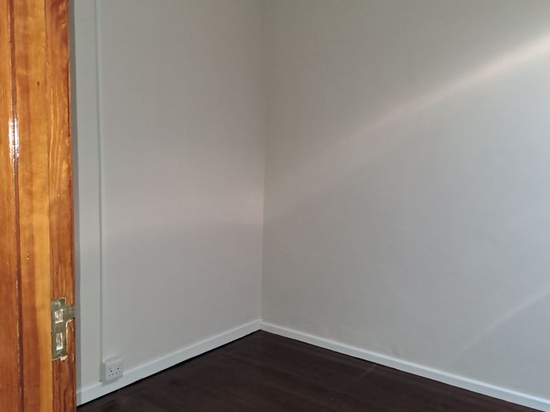A close-up view of a corner showing a wooden door frame, white walls, and dark laminate flooring.