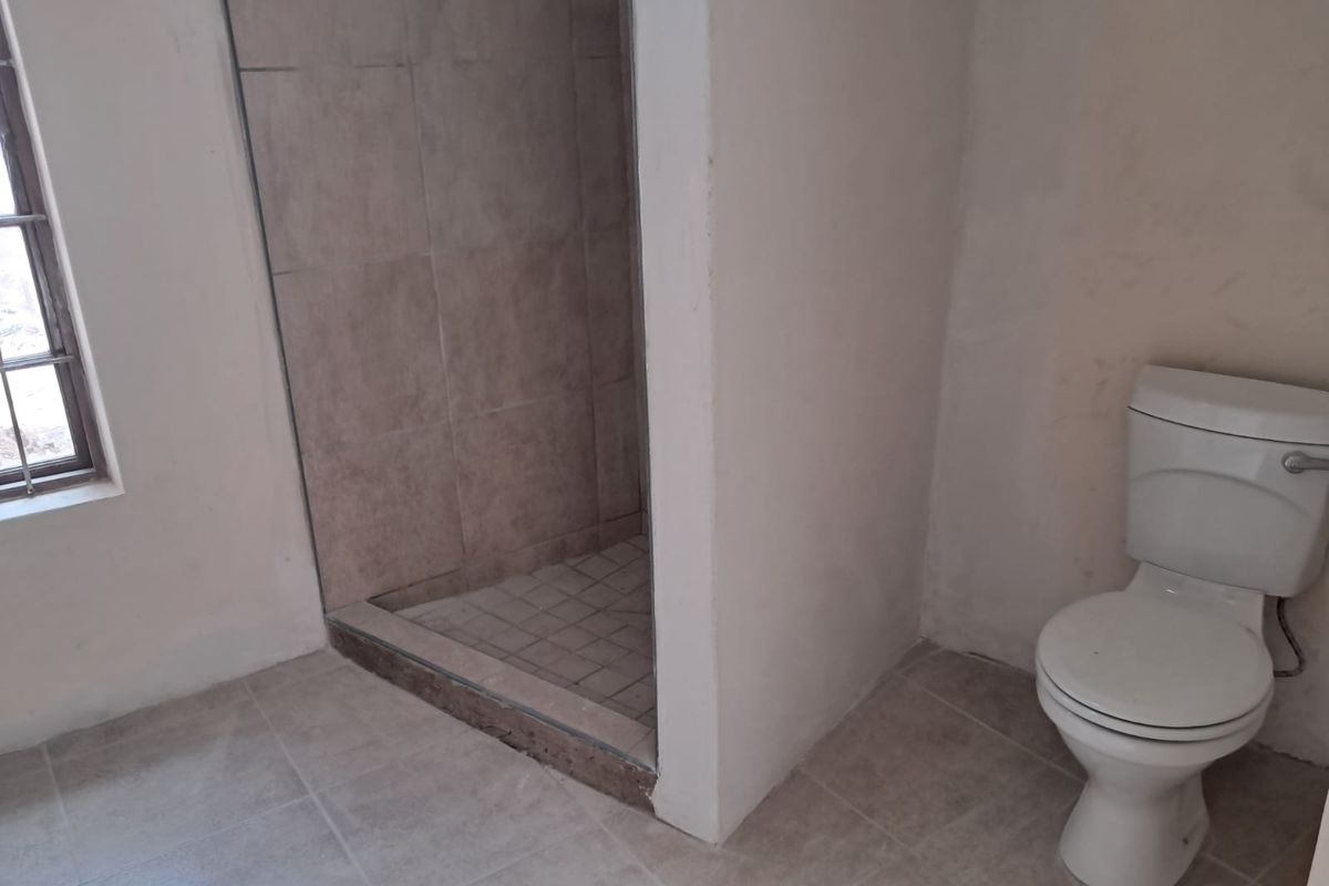 A basic bathroom featuring a tiled shower enclosure and a standard toilet, currently in need of cosmetic updates and finishing touches.