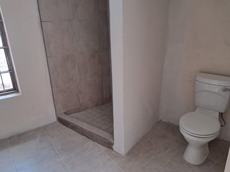 A basic bathroom featuring a tiled shower enclosure and a standard toilet, currently in need of cosmetic updates and finishing touches.