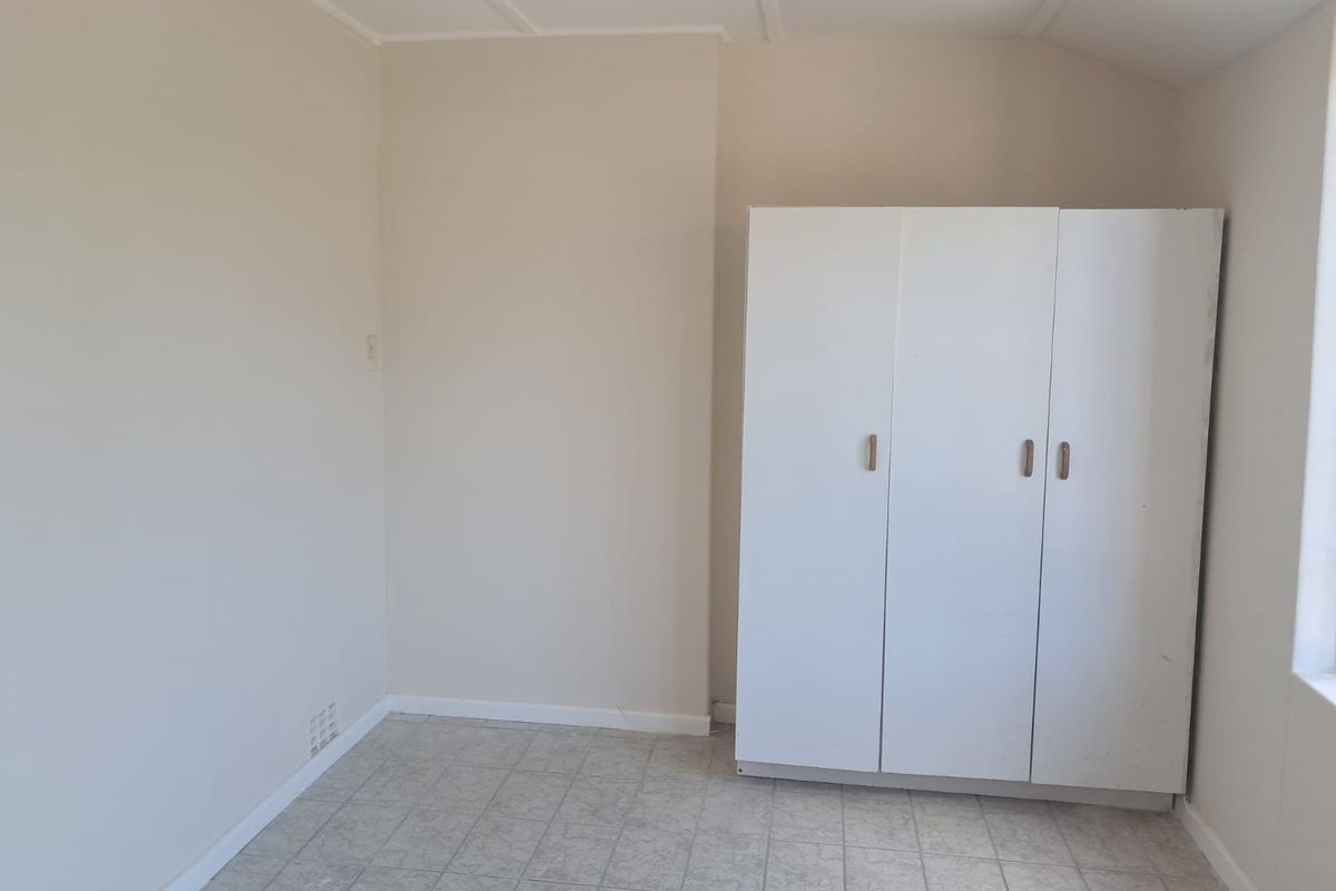 A simple, empty bedroom featuring tiled flooring and a built-in white wardrobe, offering a blank canvas for potential updates or staging.