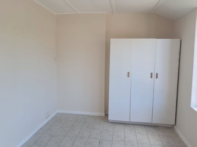 A simple, empty bedroom featuring tiled flooring and a built-in white wardrobe, offering a blank canvas for potential updates or staging.