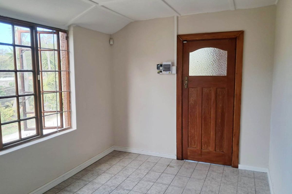 An empty living area featuring tiled flooring, a timber-framed window, and a classic wooden door with a glass panel.