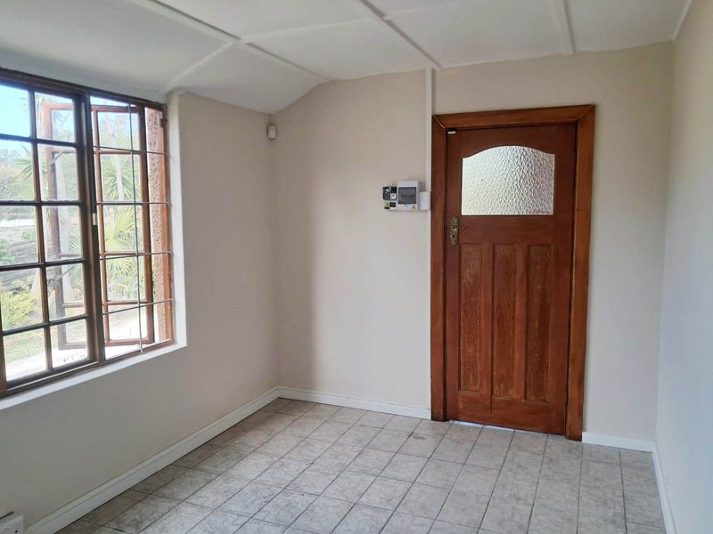An empty living area featuring tiled flooring, a timber-framed window, and a classic wooden door with a glass panel.
