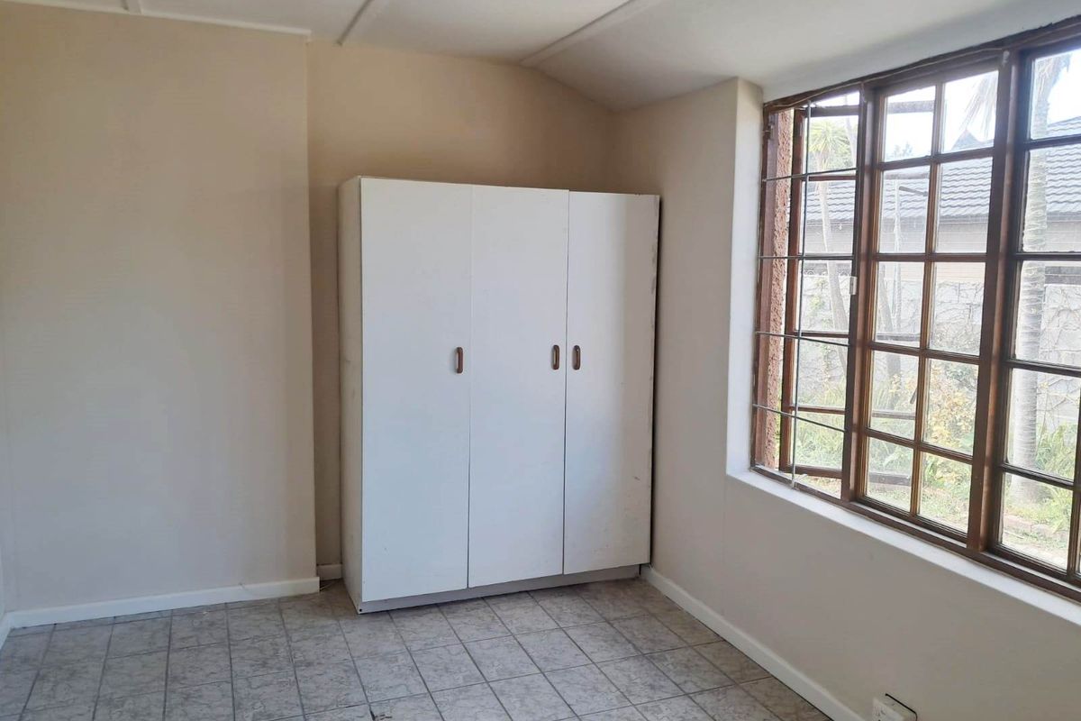 A simple bedroom featuring tiled flooring, a built-in cupboard, and a timber-framed window with security bars, offering a blank canvas for renovation.