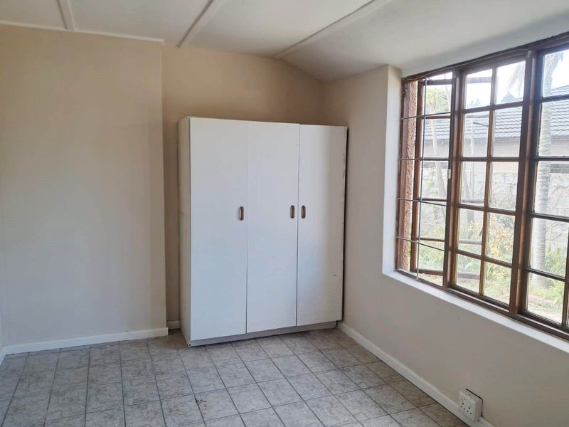 A simple bedroom featuring tiled flooring, a built-in cupboard, and a timber-framed window with security bars, offering a blank canvas for renovation.