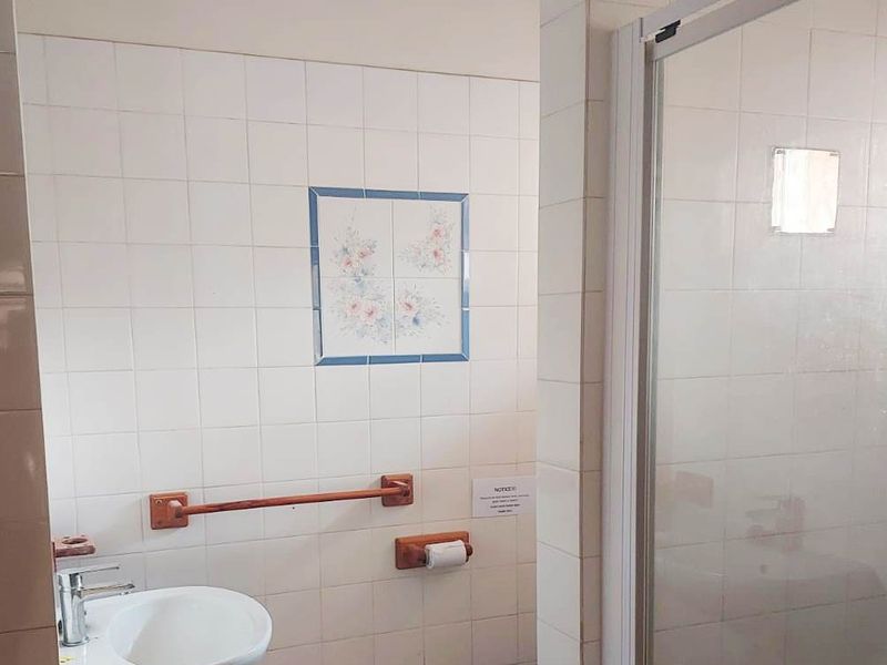 A functional bathroom featuring a wall-mounted basin, a shower enclosure, and tiled walls with decorative accents, requiring some cosmetic updates.