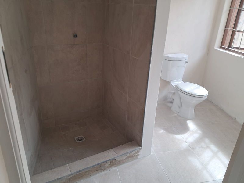 A functional bathroom featuring a tiled shower enclosure and a standard toilet, currently requiring finishing touches to the shower threshold and fixtures.