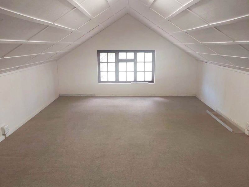 An empty attic-style bedroom featuring a pitched ceiling with exposed beams, carpeted flooring, and a multi-pane window providing natural light.
