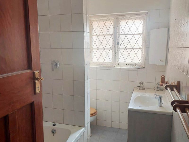 A functional bathroom featuring a built-in bathtub, shower fixture, and vanity basin with tiled finishes and security bars on the window.