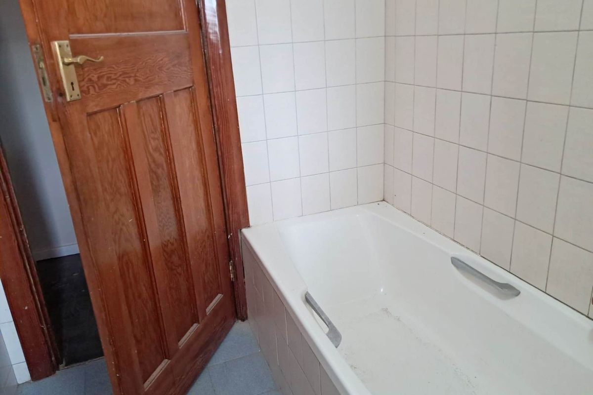 A dated bathroom featuring a standard bathtub with tiled surround and a traditional timber door.