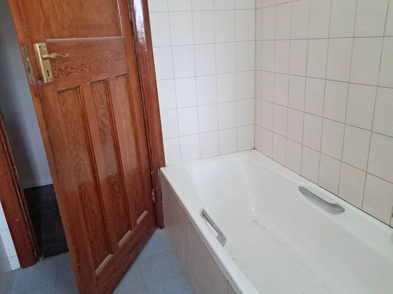 A dated bathroom featuring a standard bathtub with tiled surround and a traditional timber door.