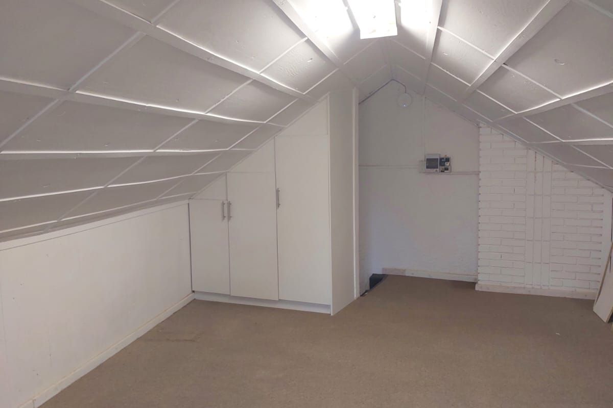 An empty attic-style bedroom featuring sloped ceilings, built-in storage cabinetry, and exposed brickwork, offering a versatile space for renovation.