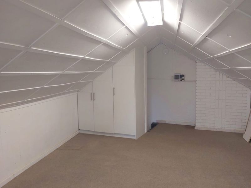 An empty attic-style bedroom featuring sloped ceilings, built-in storage cabinetry, and exposed brickwork, offering a versatile space for renovation.