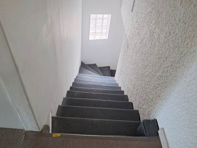 A narrow interior staircase featuring grey carpeted steps and a small glass block window, showing signs of wear on the floor coverings.