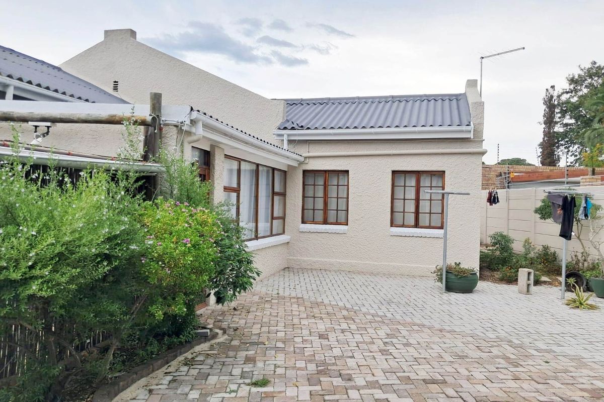 A rear exterior view of the property featuring a paved courtyard area, plastered walls, and timber-framed windows under a corrugated metal roof.