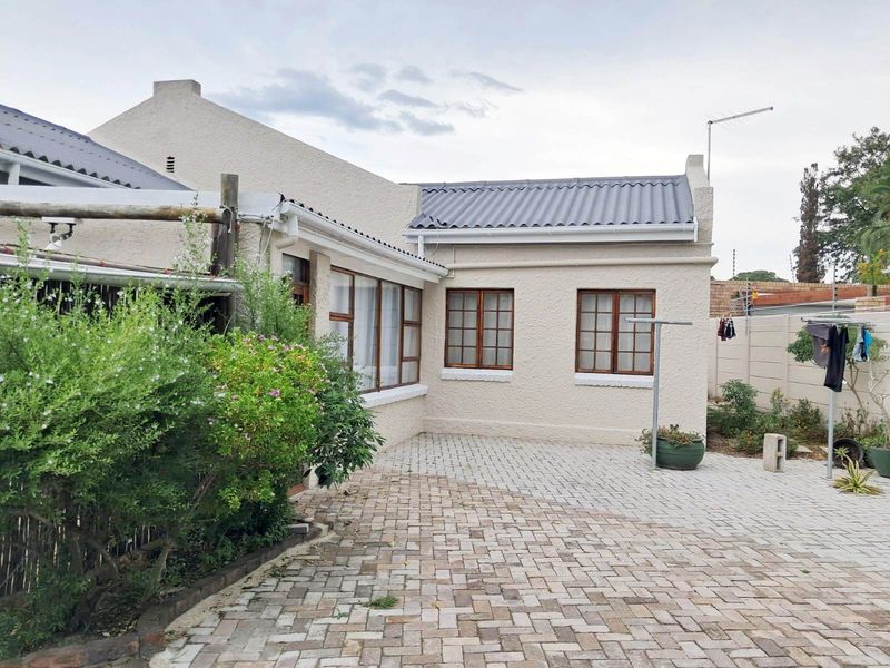 A rear exterior view of the property featuring a paved courtyard area, plastered walls, and timber-framed windows under a corrugated metal roof.