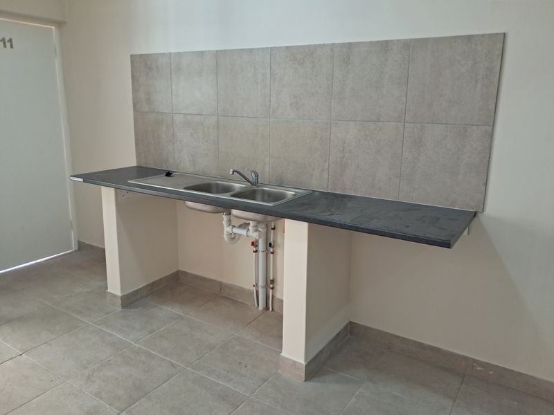 A clean, functional laundry area featuring a double stainless steel sink, tiled splashback, and durable laminate countertop with exposed plumbing connections.