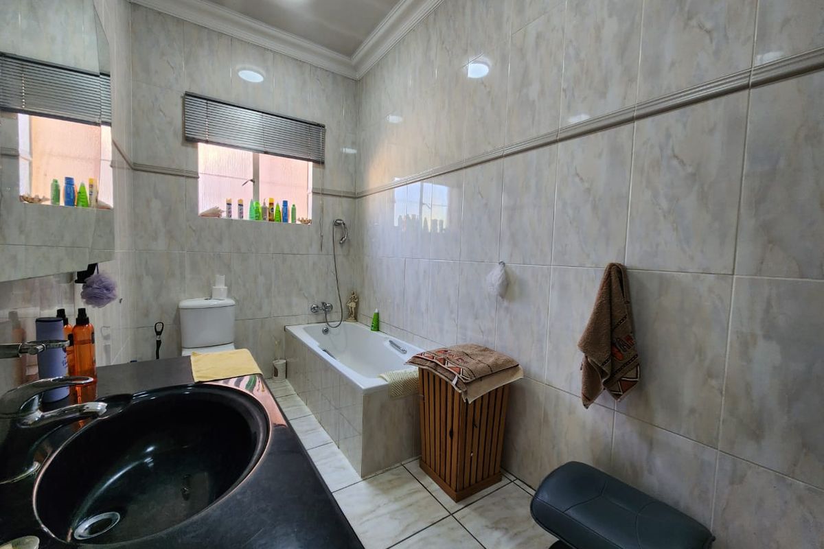 A functional bathroom featuring a built-in bathtub, a vanity with a dark countertop, and full-height wall tiling.