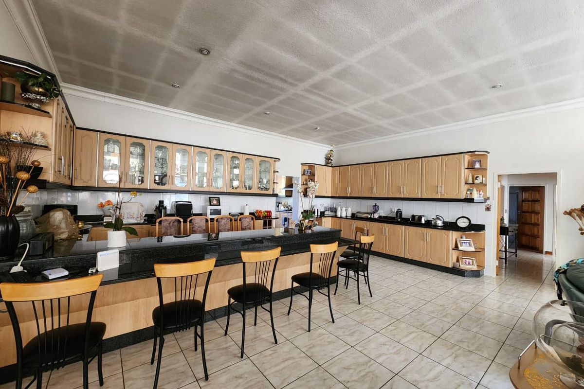 Spacious kitchen featuring extensive light wood cabinetry, black granite countertops, a large breakfast bar, and tiled flooring throughout.