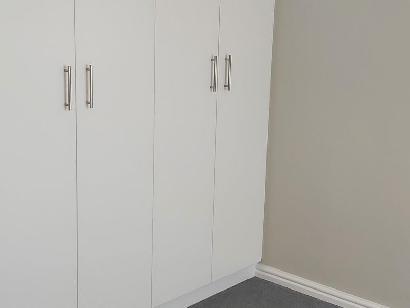 A clean, empty bedroom corner featuring modern white built-in cupboards, neutral wall paint, and grey carpet flooring.