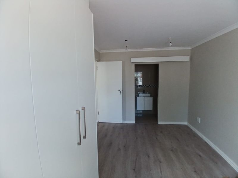 A clean, empty bedroom featuring modern laminate flooring, built-in wardrobes, and direct access to an en-suite bathroom.
