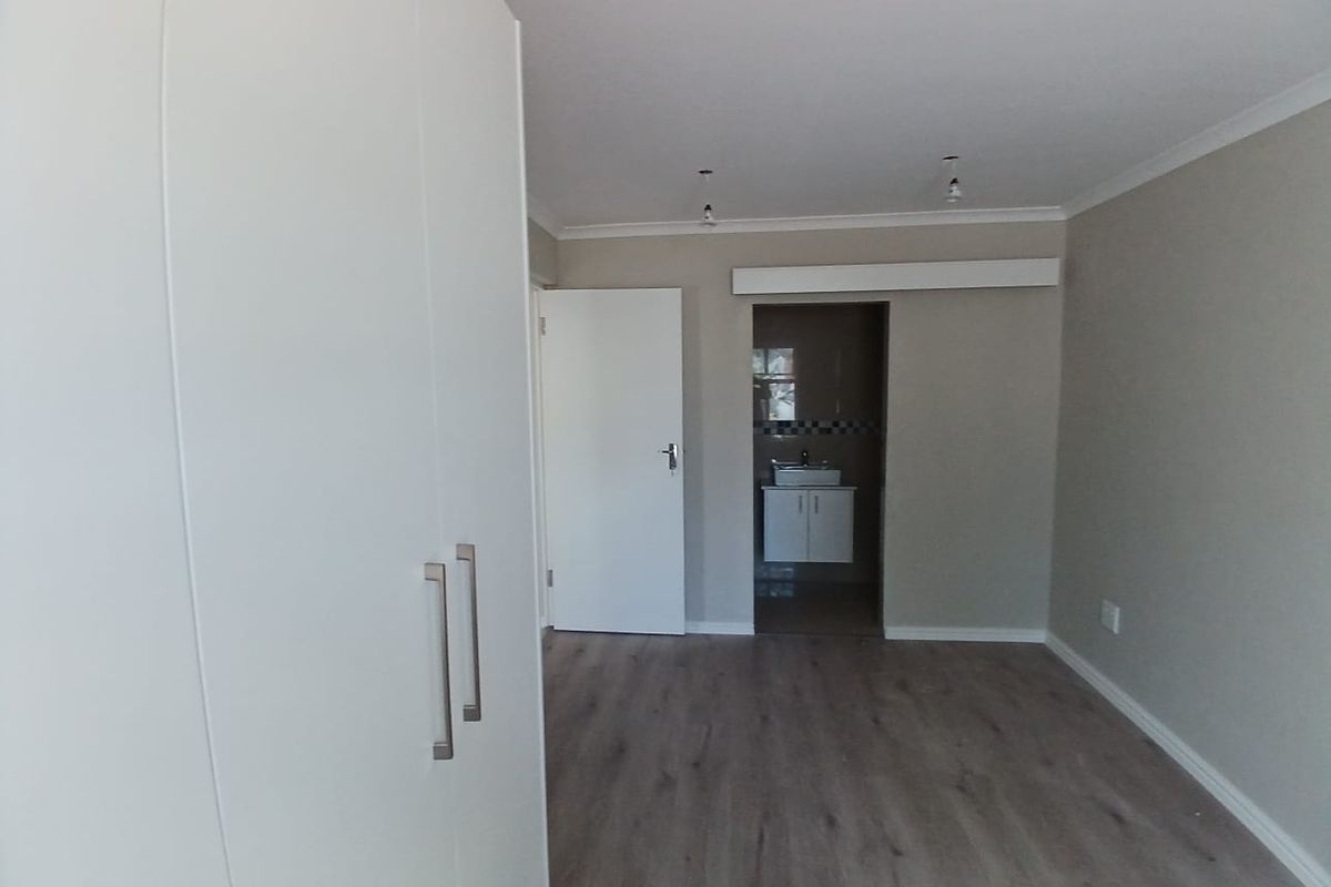A clean, empty bedroom featuring modern laminate flooring, built-in wardrobes, and direct access to an en-suite bathroom.