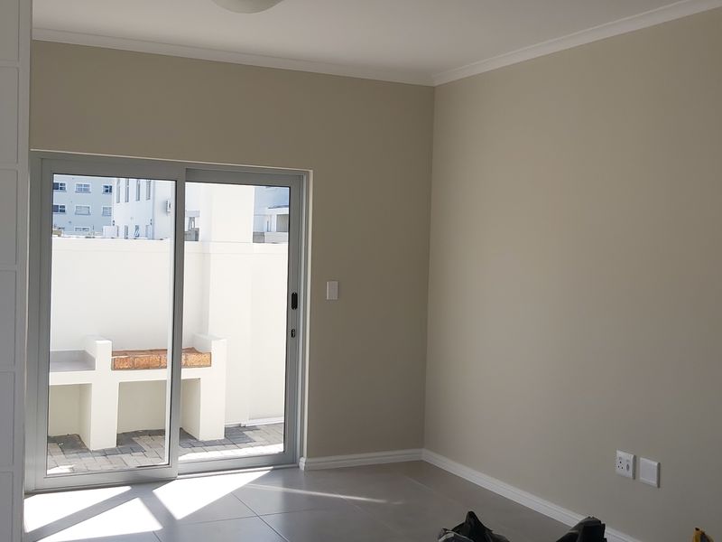 A bright, empty living room featuring neutral walls, tiled flooring, and a sliding glass door providing access to an outdoor patio area.