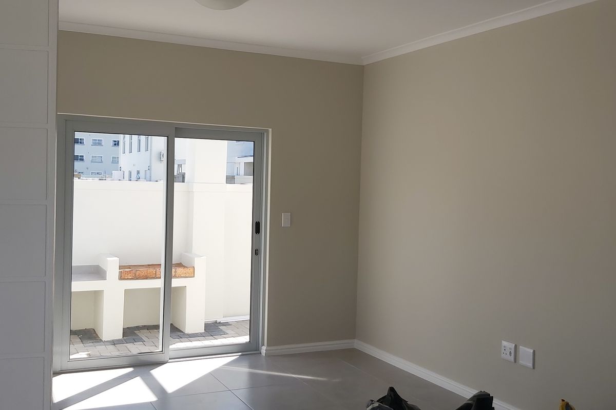 A bright, empty living room featuring neutral walls, tiled flooring, and a sliding glass door providing access to an outdoor patio area.