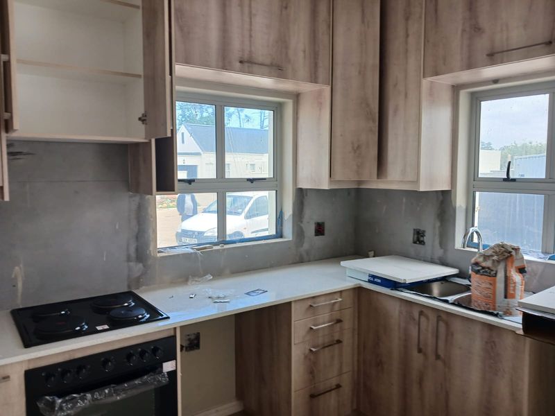 An unfinished kitchen featuring wood-look cabinetry, a built-in oven and hob, and stone countertops, currently awaiting final wall finishes and electrical completion.