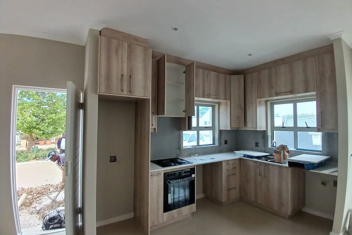 A modern kitchen in the final stages of completion, featuring light wood-tone cabinetry, built-in oven, hob, and direct access to the exterior.