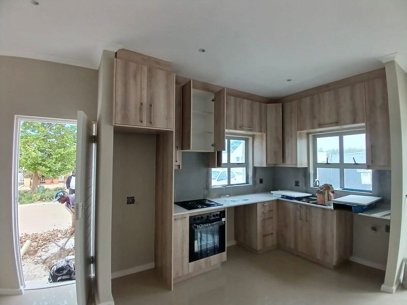 A modern kitchen in the final stages of completion, featuring light wood-tone cabinetry, built-in oven, hob, and direct access to the exterior.