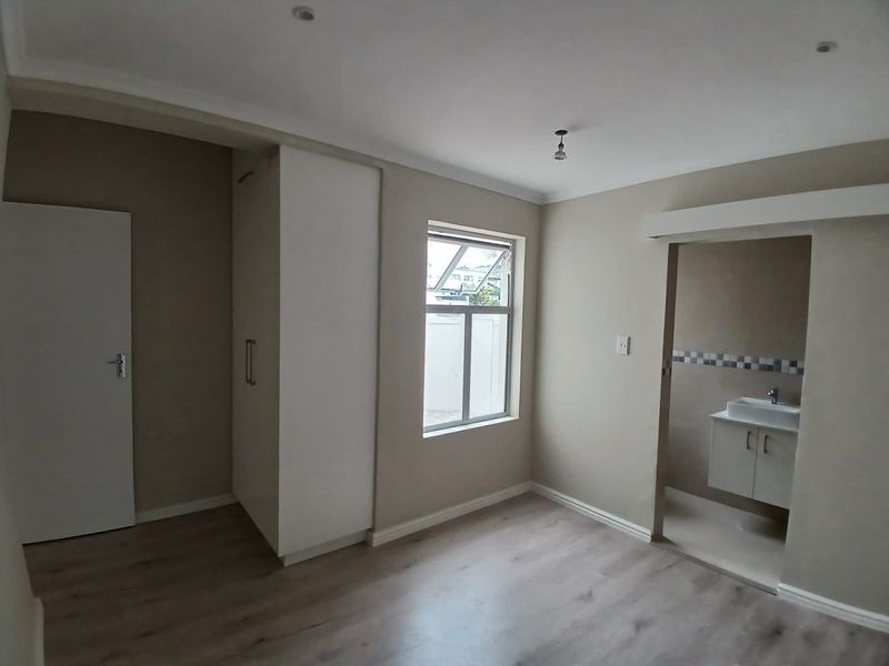 A clean, empty bedroom featuring laminate flooring, built-in cupboards, and an attached en-suite bathroom with a modern vanity basin.