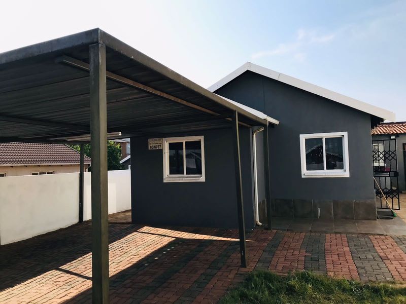 Exterior view of the property featuring a covered carport, paved driveway, and dark grey painted facade with white window frames.