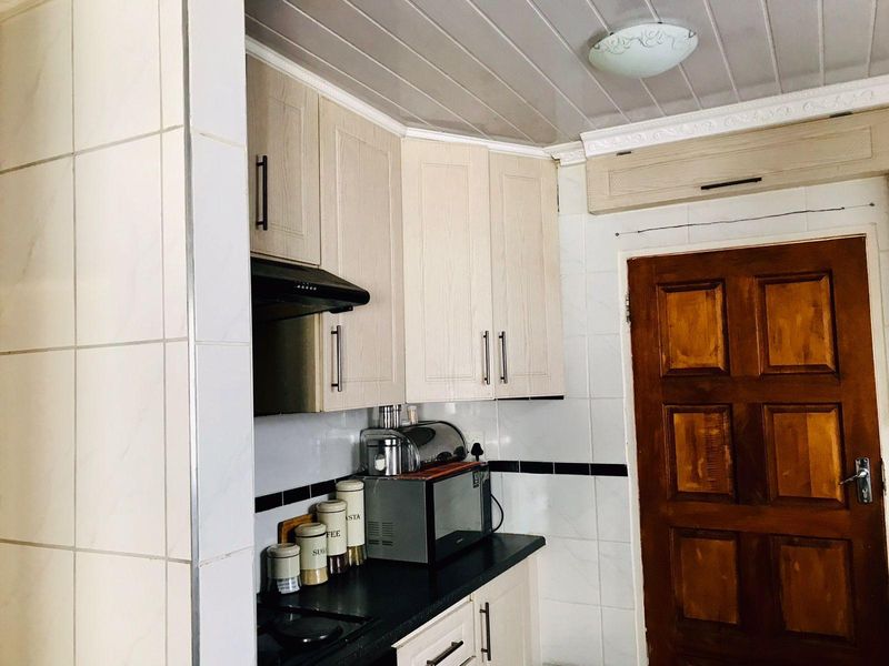 A compact kitchen featuring light-toned cabinetry, dark countertops, tiled splashbacks, and a traditional timber door.