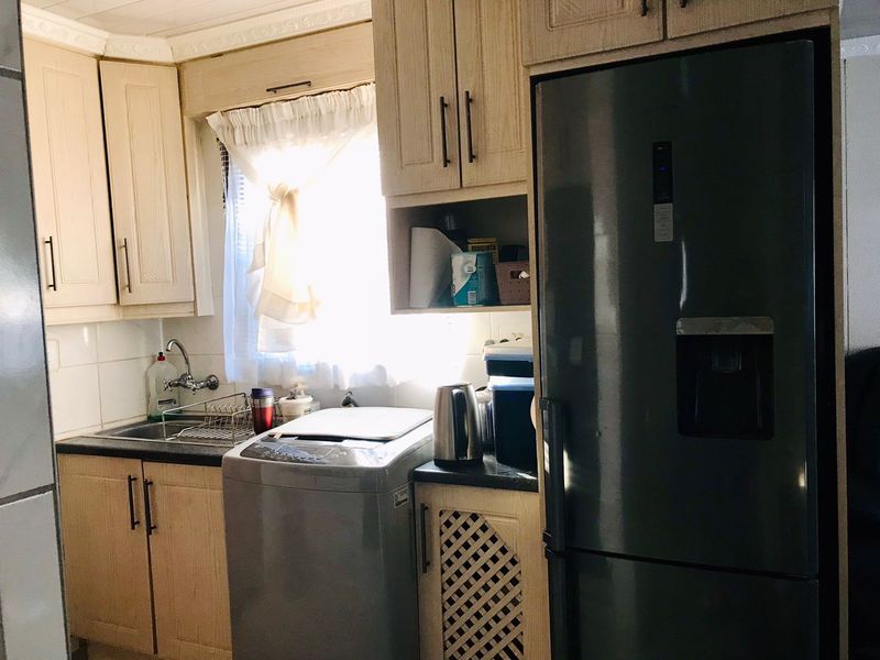 A functional kitchen featuring light wood-look cabinetry, dark countertops, a tiled backsplash, and a stainless steel sink with a mixer tap.