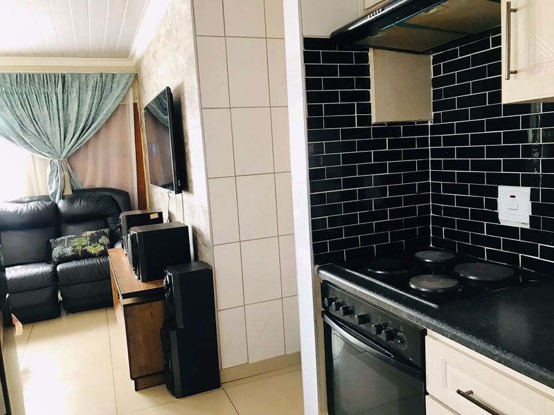 Open plan living area featuring a compact kitchen with black subway tile splashback, built-in oven, and hob, adjacent to a comfortable lounge space.